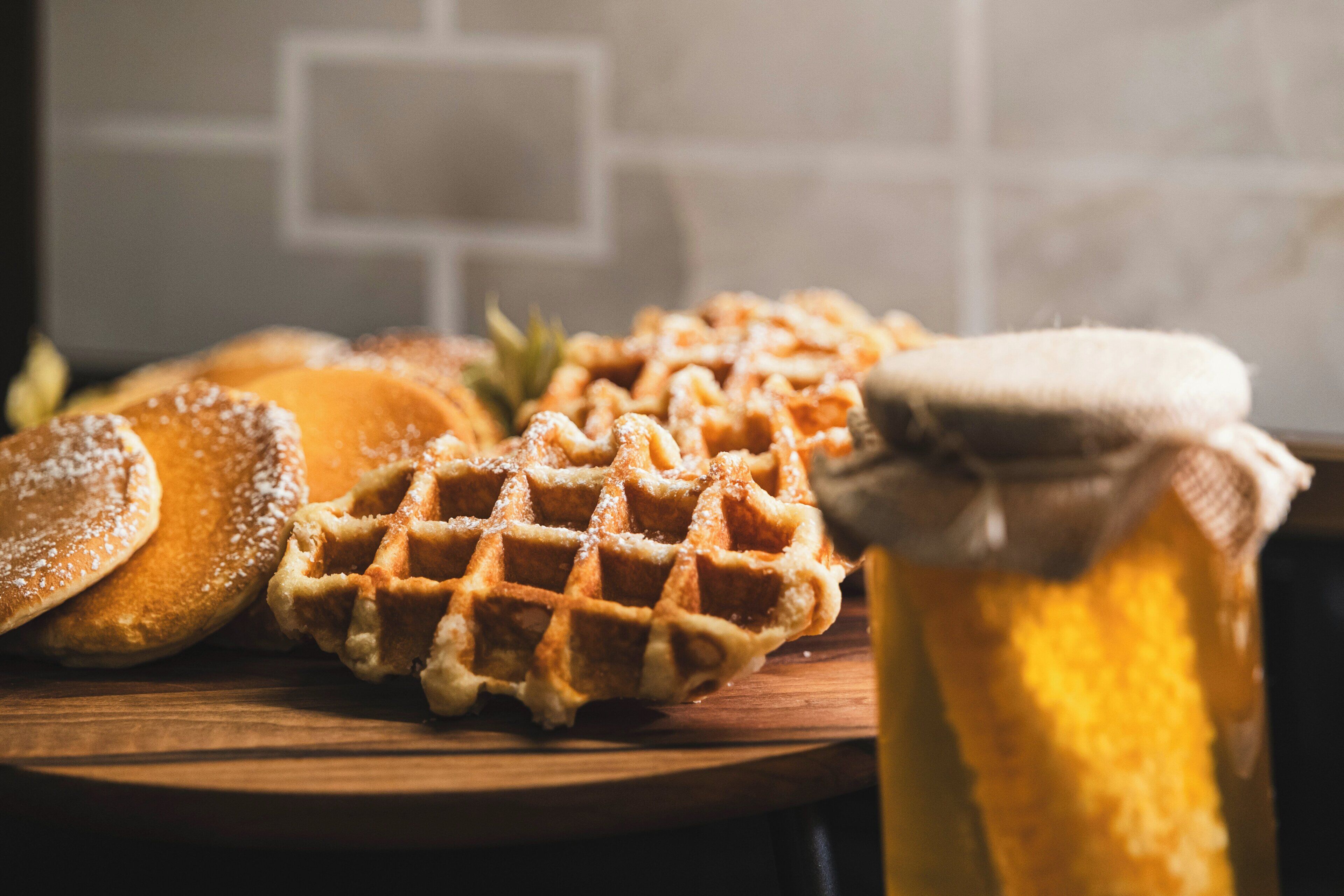 A wooden board with waffles, pancakes, and a jar of honey.