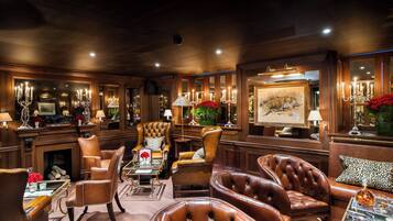 A luxurious lounge area with leather armchairs, a fireplace, and elegant decor including a large painting and candelabras.