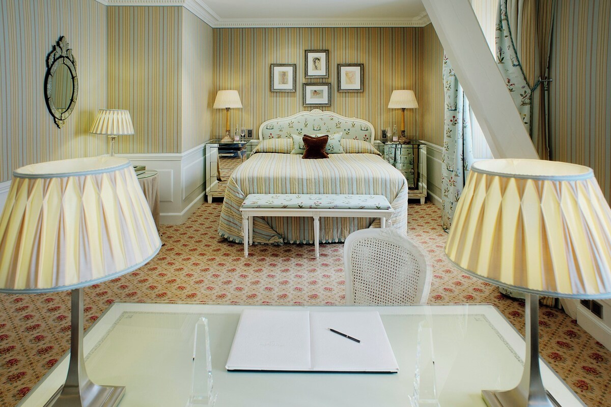 A bedroom with a bed, two bedside tables, a bench, a desk with a chair, and a mirror on the wall.