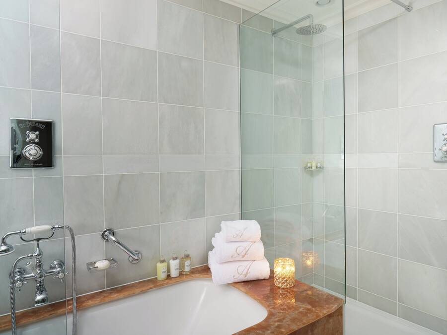 Un baño moderno con ducha envuelta en vidrio, lavamanos de mármol y toallas ordenadamente dobladas.