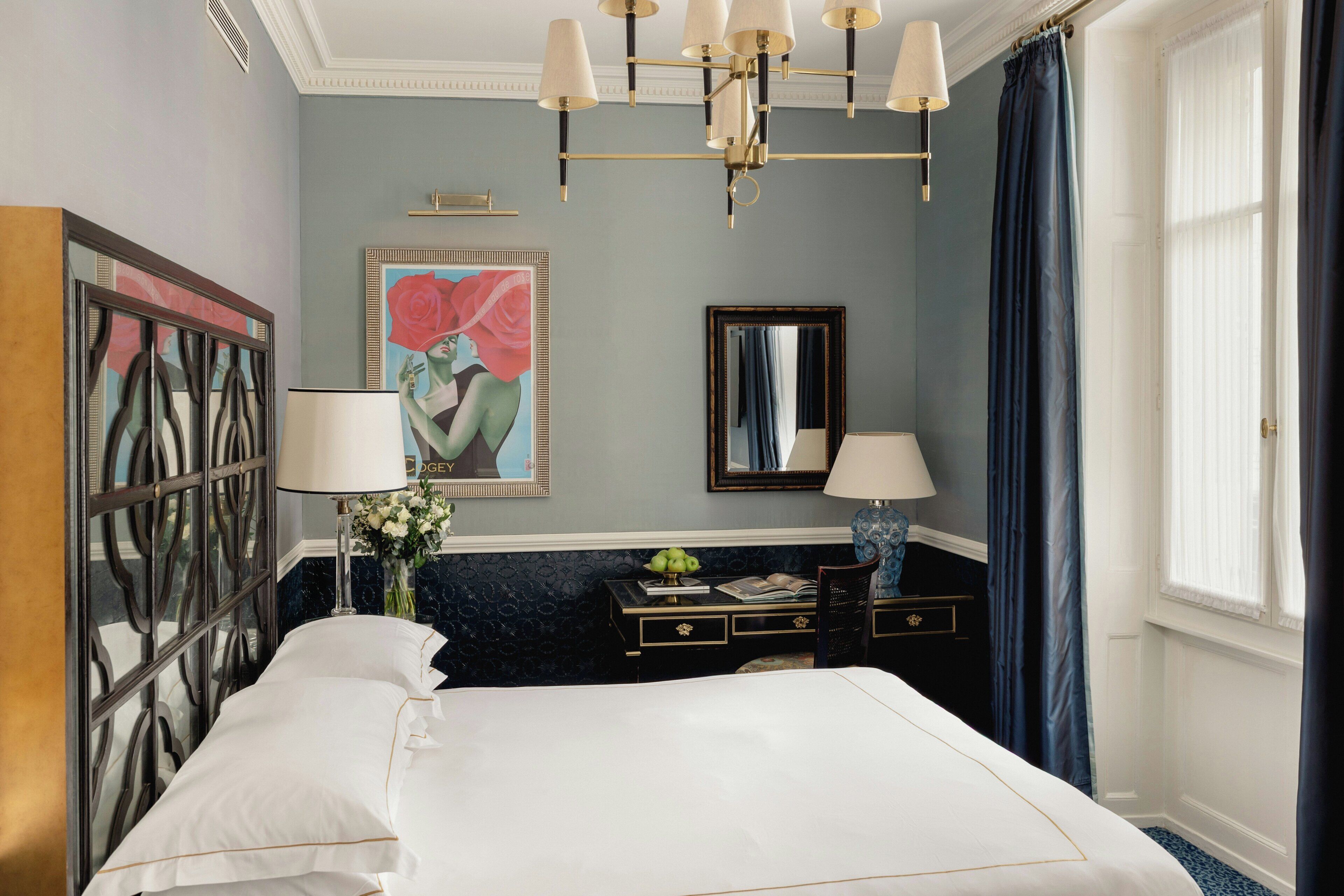 A hotel room with a large bed, a desk with a lamp, a mirror, and a painting on the wall.