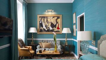 A room with teal walls, a large abstract painting, a sofa, two armchairs, a coffee table, and a bed.