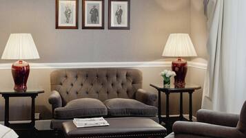 Una habitación con un sillón capitoné, dos mesitas de noche con lámparas y cuadros en la pared.
