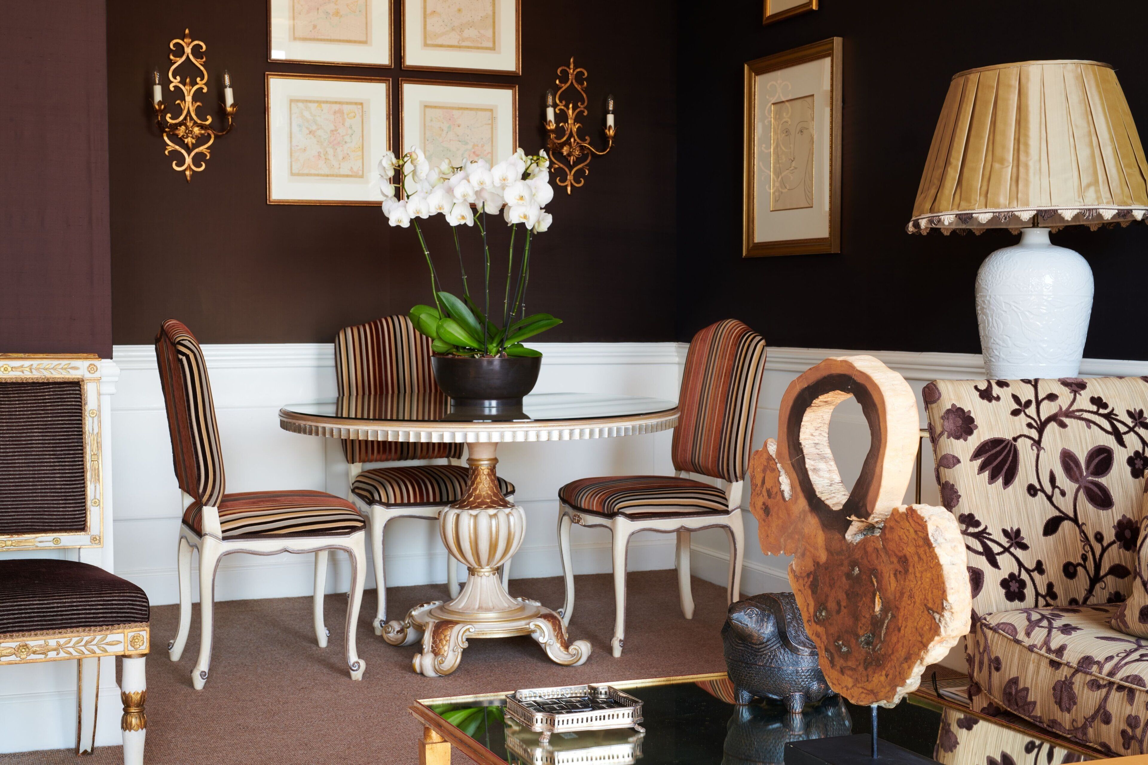 A room with a round table, striped chairs, a sofa, and a decorative lamp.
