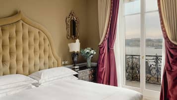 Ein Hotelzimmer mit einem großen Bett, einem Schminktisch, einem Spiegel und Blick auf eine Stadtlandschaft durch ein Fenster mit Vorhängen.