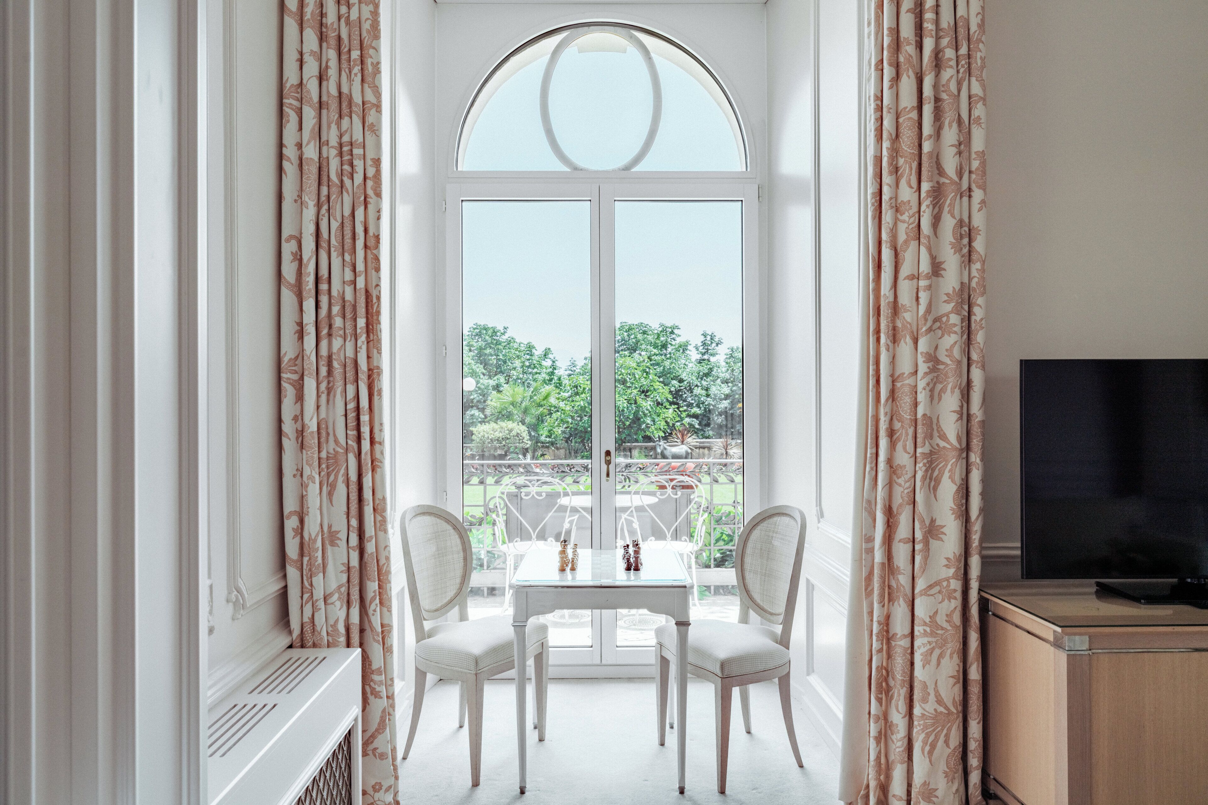 A room with a large arched window, a white table with chairs, and a television on a wooden cabinet.