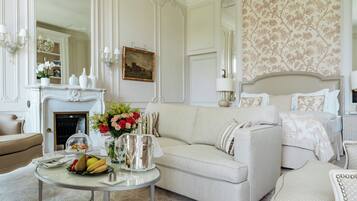 Una habitación elegante con chimenea, un sofá, una mesa de comedor con fruta y flores, y una cama con edredón estampado con motivos florales.