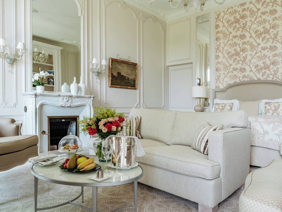 Una habitación elegante con chimenea, un sofá, una mesa de comedor con fruta y flores, y una cama con edredón estampado con motivos florales.