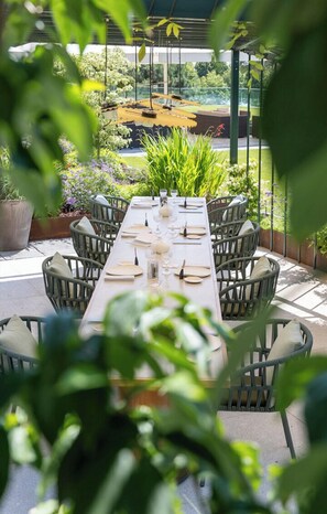 A covered outdoor dining area with a long table set for six, surrounded by wicker chairs.