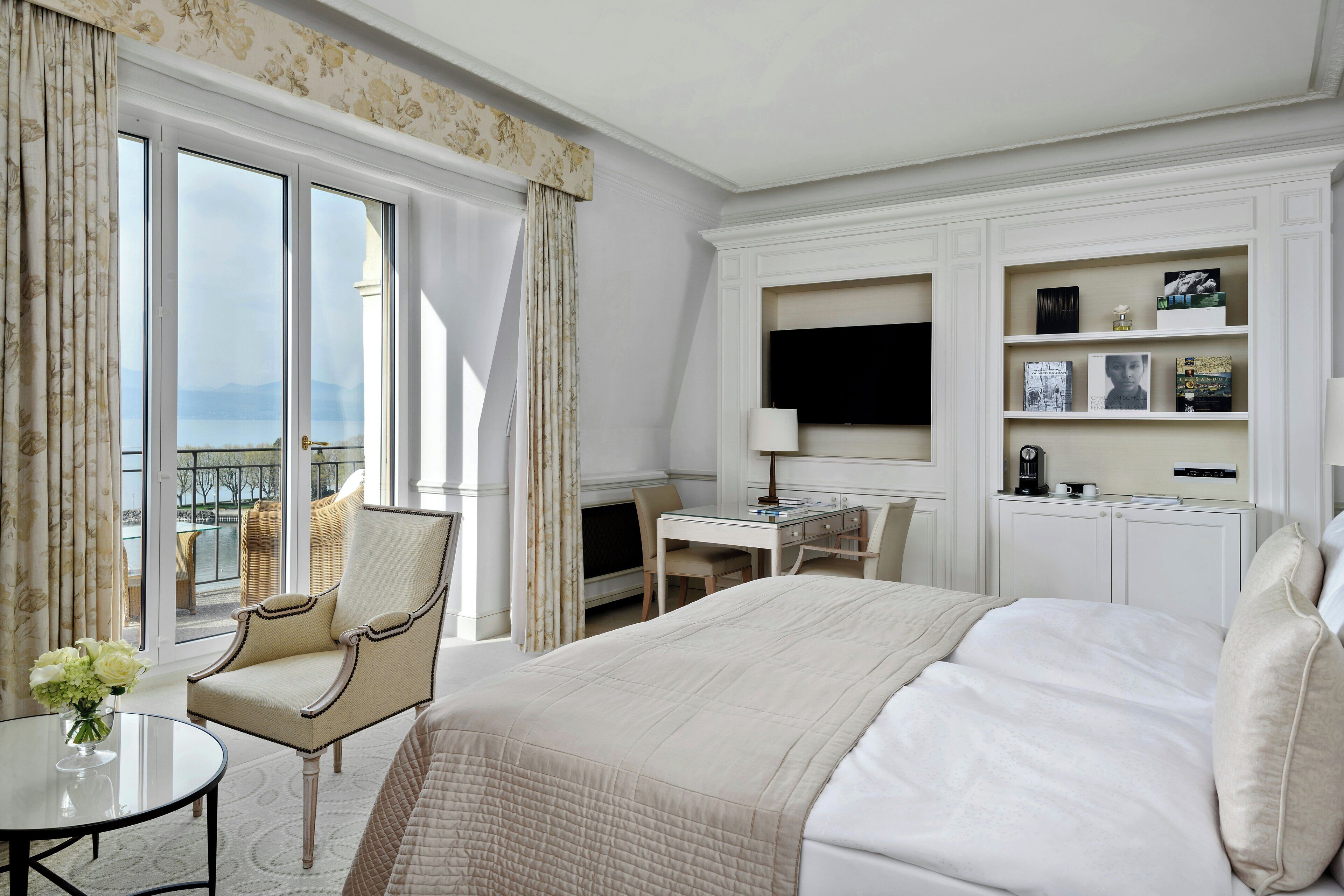 Habitación de hotel con una cama grande, un escritorio, una silla, un televisor y un balcón con vistas.
