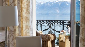 A balcony with wicker furniture, a glass table, and a view of a lake and mountains. - Beau-Rivage Palace (Lausanne)