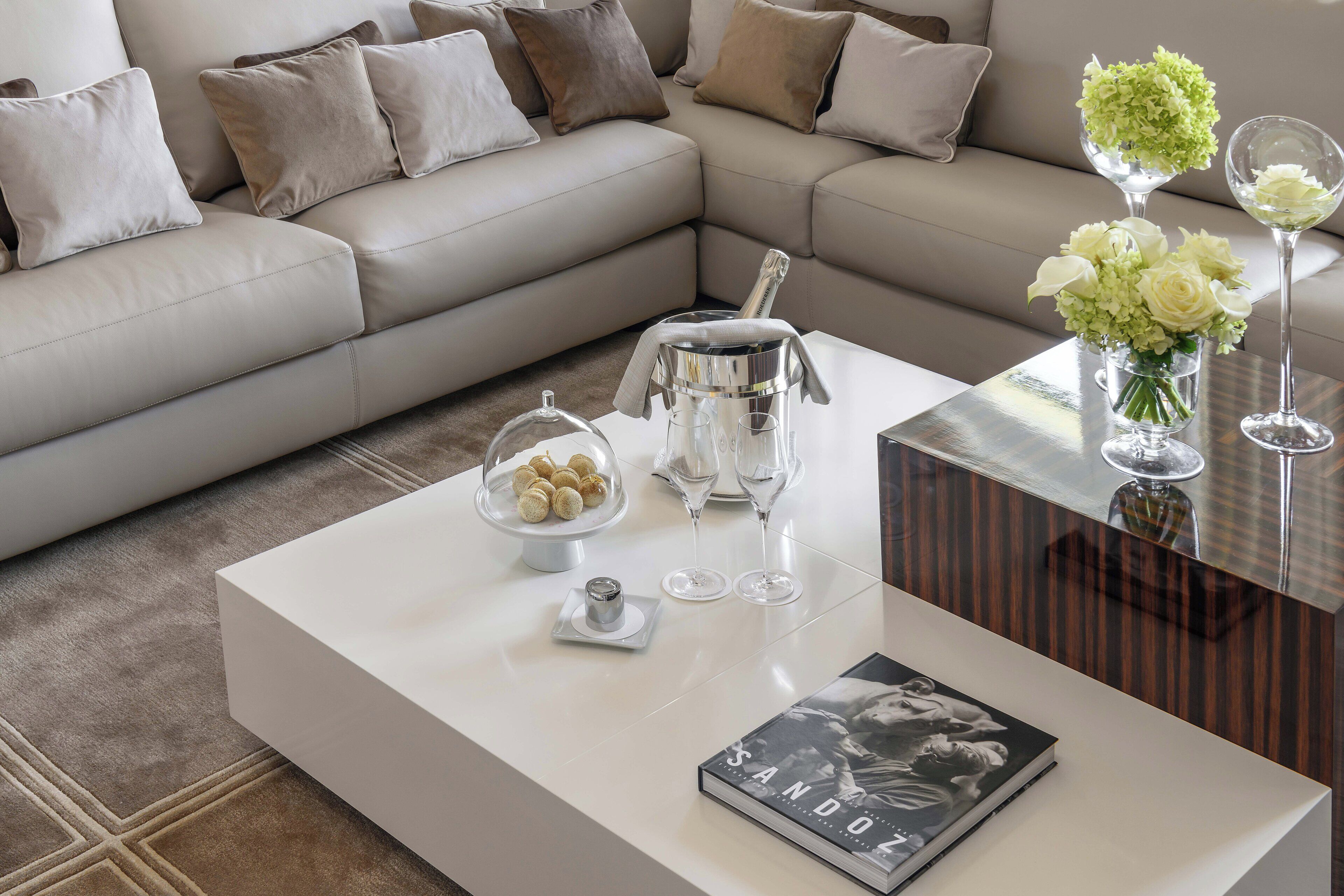 A modern living room with a beige sofa, a white coffee table, and a glass vase with flowers.
