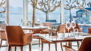 A restaurant with tables set for dining, large windows with a view of a tree and a body of water. - Beau-Rivage Palace (Lausanne)