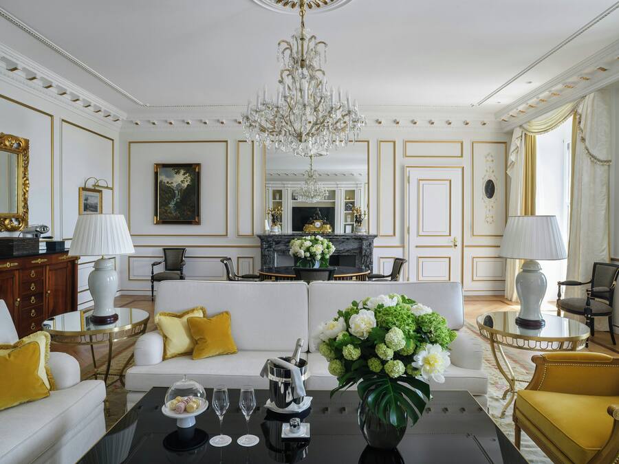 Un salón lujoso con candelabro, sofás blancos con cojines amarillos, chimenea y zona de comedor.