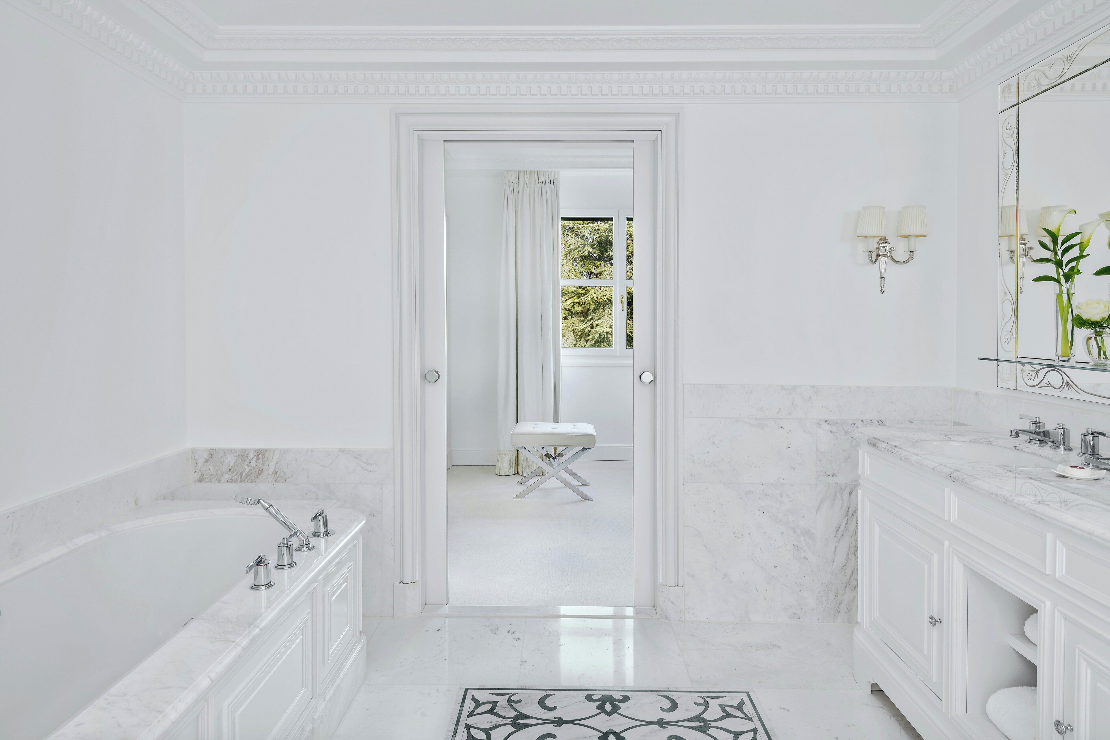 A bathroom with a bathtub, a vanity with a mirror, and a door leading to a room with a window.