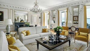 A luxurious living room with a chandelier, a sofa set, a coffee table, and a view of the sea. - Beau-Rivage Palace (Lausanne)