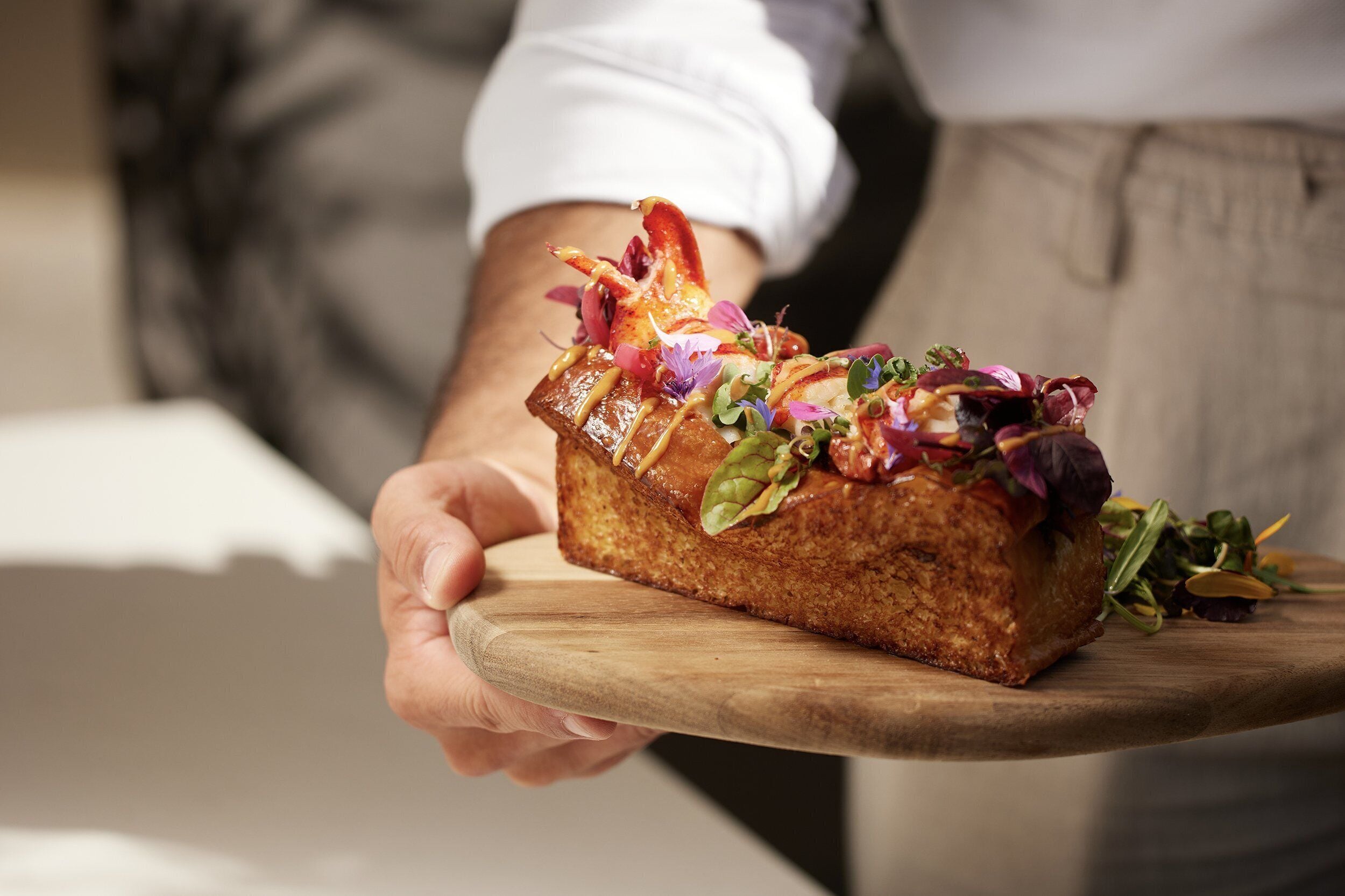 Una persona sostiene un pan con diferentes ingredientes sobre una tabla de madera.