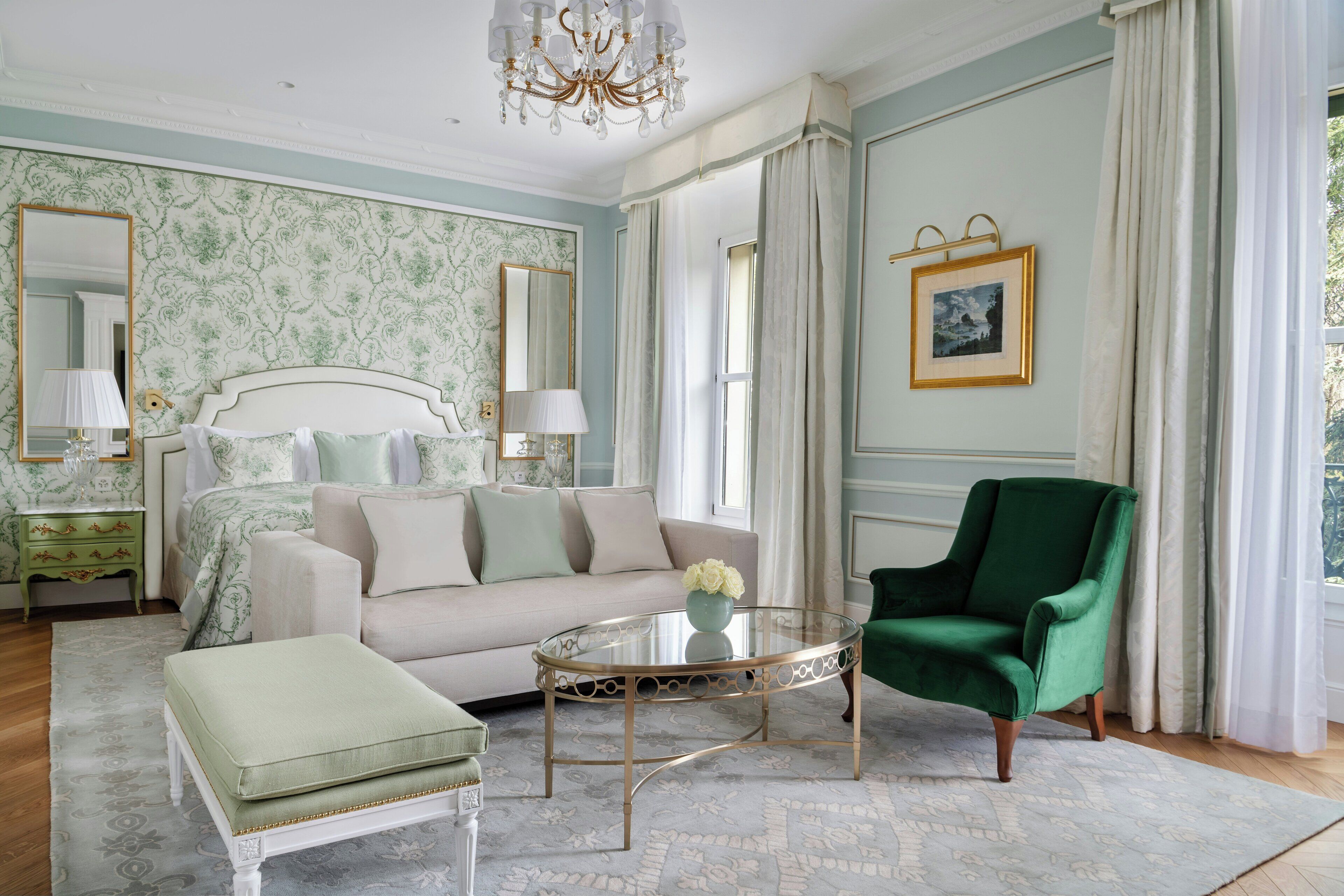 A bedroom with a bed, a green armchair, a glass coffee table, and a large mirror.