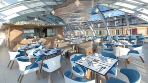 A spacious dining area with tables and chairs, a bar, and a high ceiling with a glass structure.