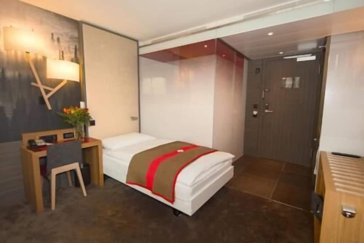 Ein Hotelzimmer mit Bett, Schreibtisch, Stuhl, Lampe und einer Tür.