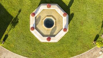 Una fuente octogonal con un elemento acuático central rodeado por un borde de piedra circular, ubicada en un césped cuidado y con un camino pavimentado alrededor.