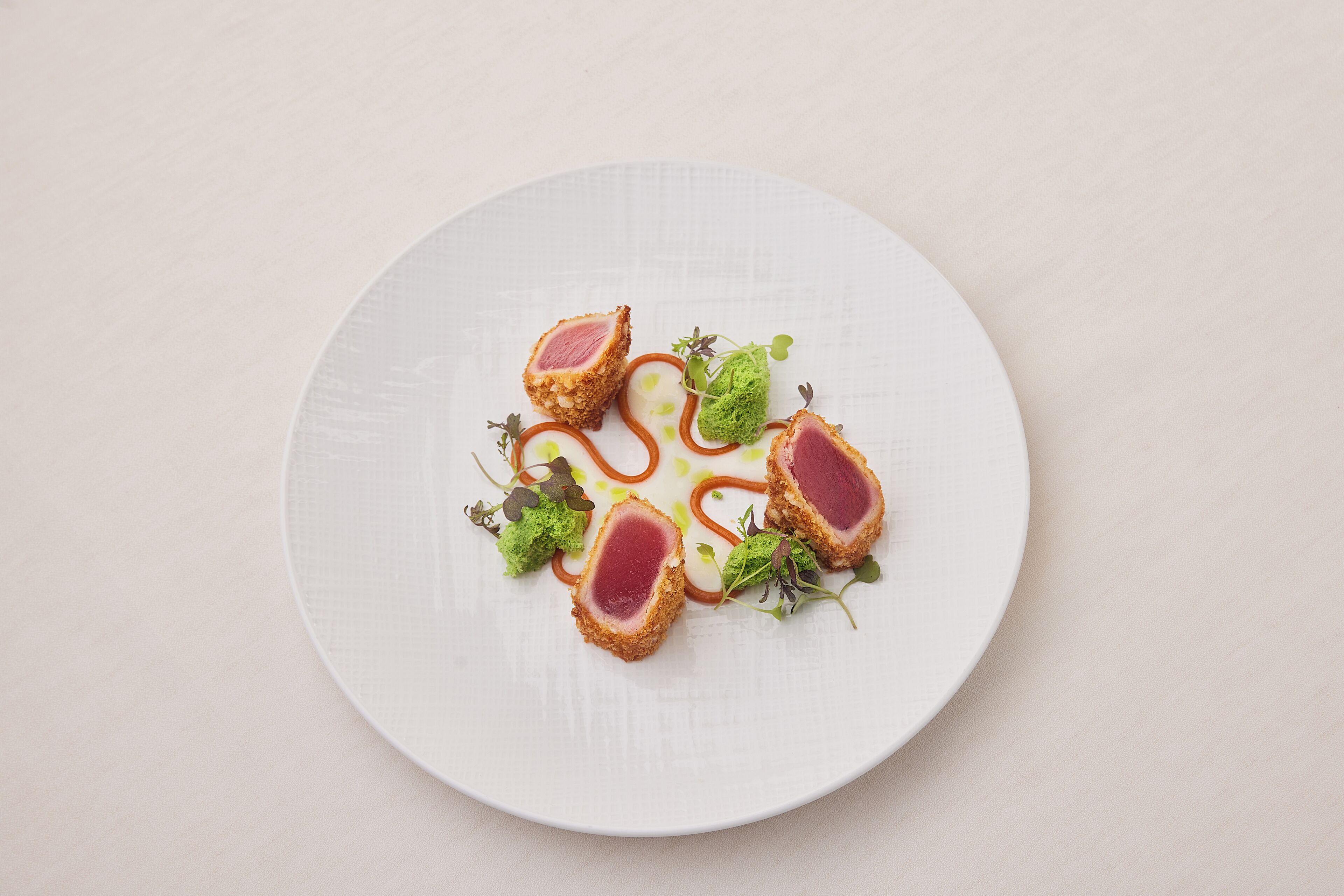 A white plate with a dish of food, including a pink center and green garnish.