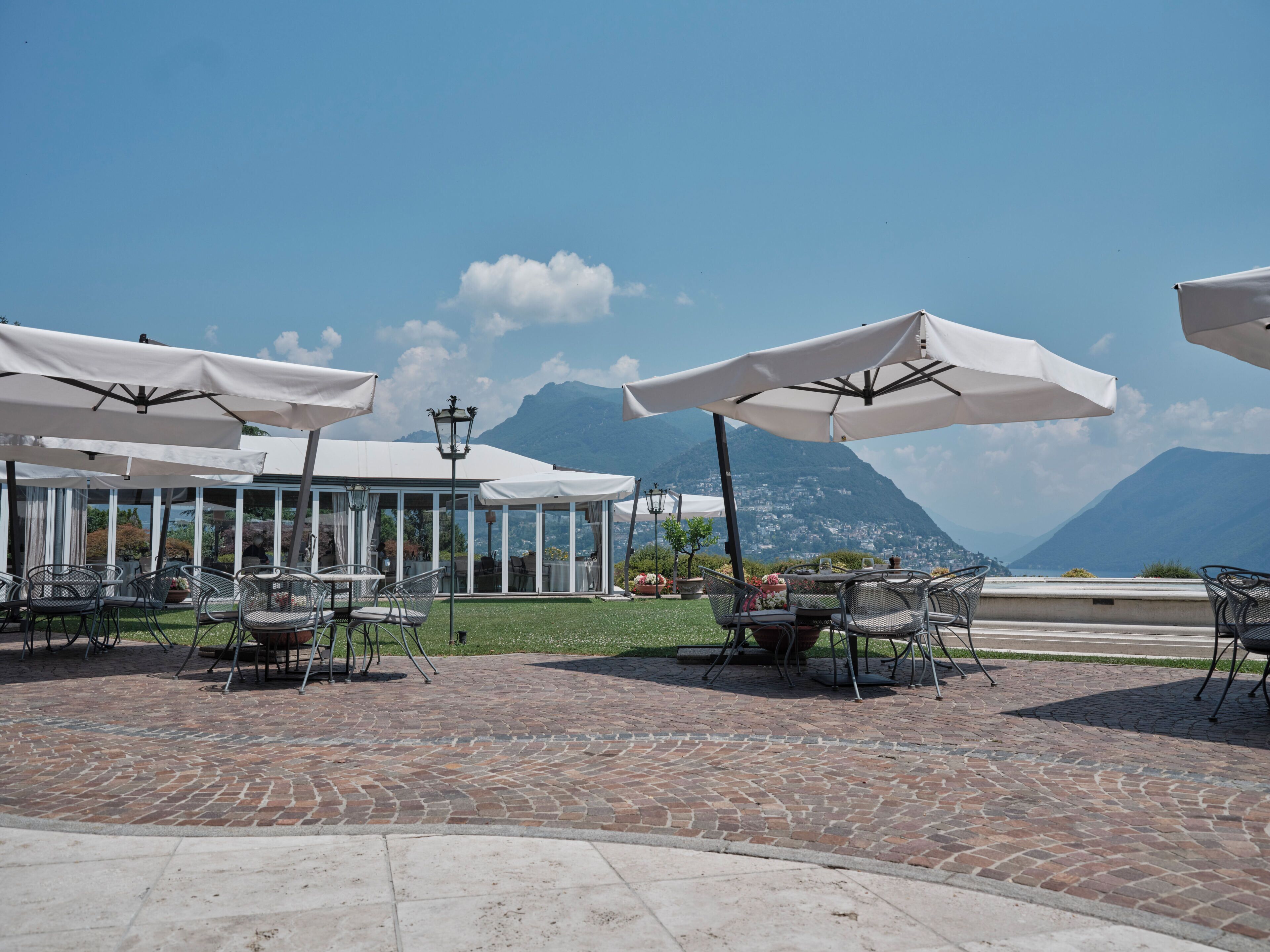 An outdoor seating area with tables and chairs, umbrellas, and a mountain view.