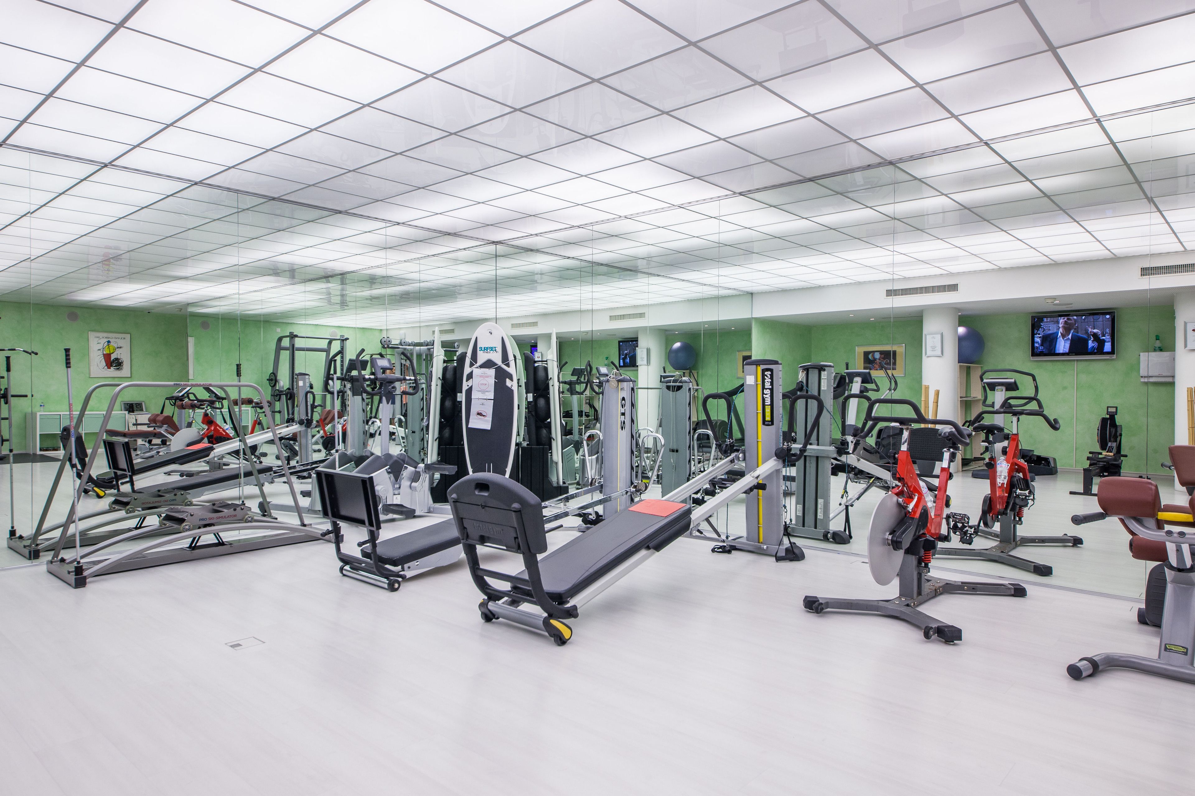 Een fitnessruimte met diverse trainingsapparaten, een spiegelwand en een televisie aan de muur.