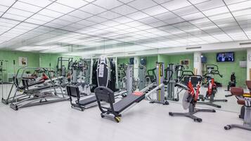 Ein Fitnessstudio mit verschiedenen Trainingsgeräten, einer Spiegelwand und einem Fernseher an der Wand.