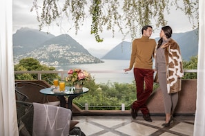 A couple standing on a balcony overlooking a lake with mountains in the background.
