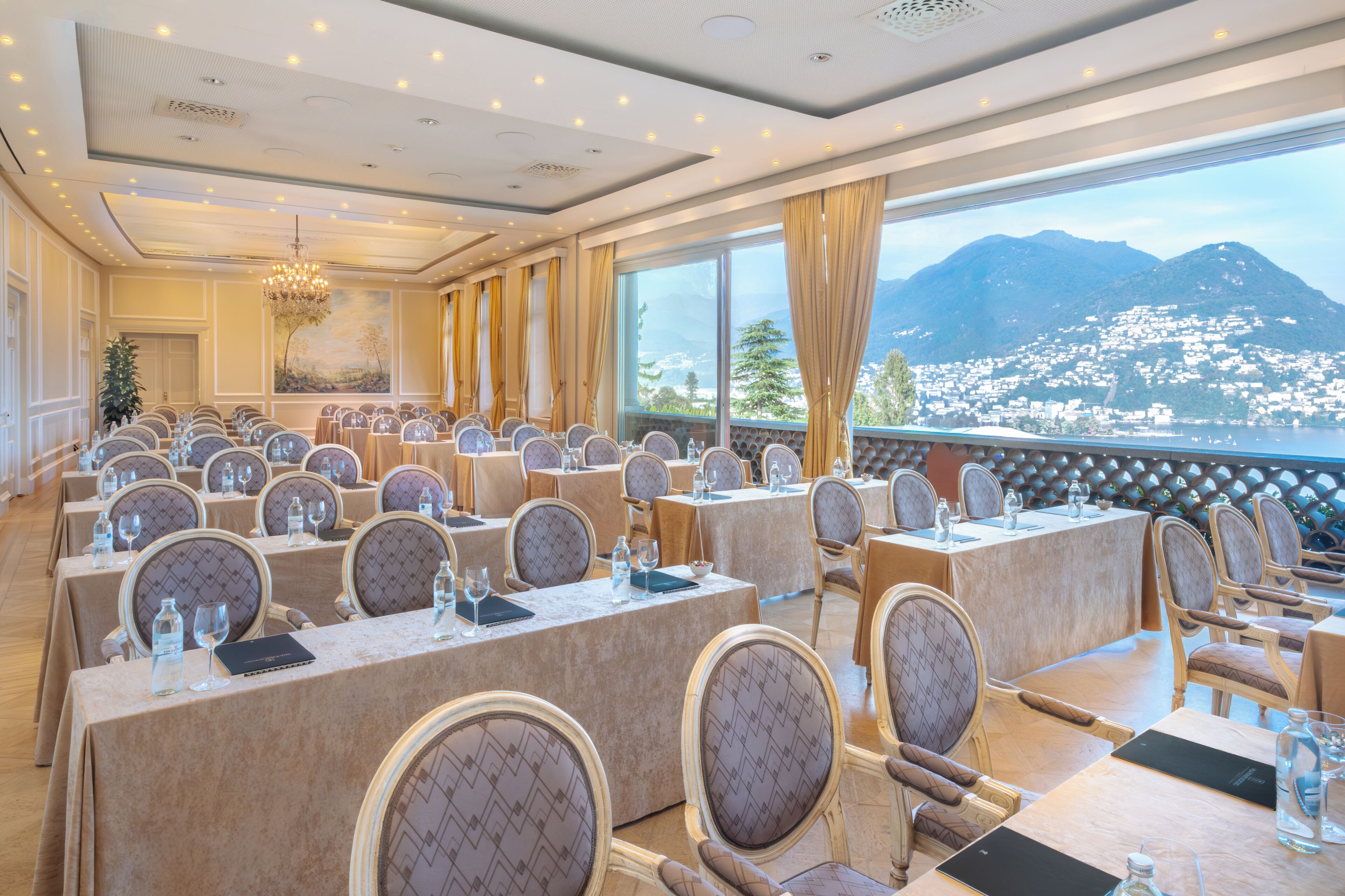 Un salón de conferencias con mesas y sillas, ventanas amplias con vista a la montaña y una araña.