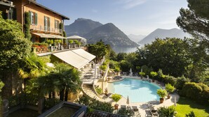 A pool area with a clear view of mountains, surrounded by lush greenery and a building with a balcony.