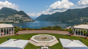 A scenic view of a lake surrounded by mountains, with a gazebo and outdoor seating area in the foreground.