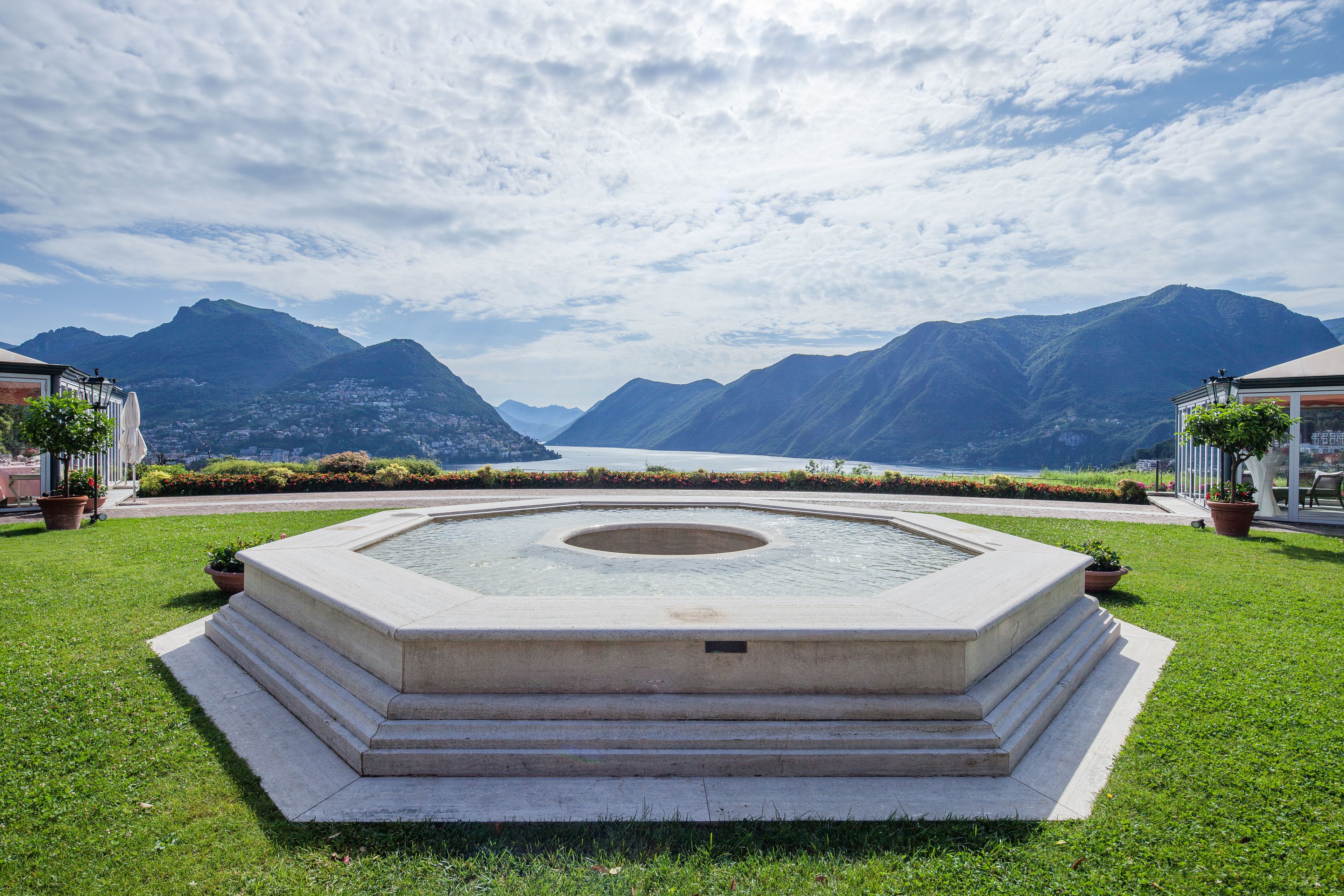 A circular water feature with steps in a landscaped area, surrounded by mountains and a clear sky.