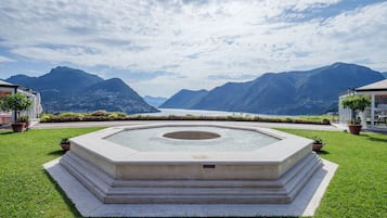 A circular water feature with steps in a landscaped area, surrounded by mountains and a clear sky.