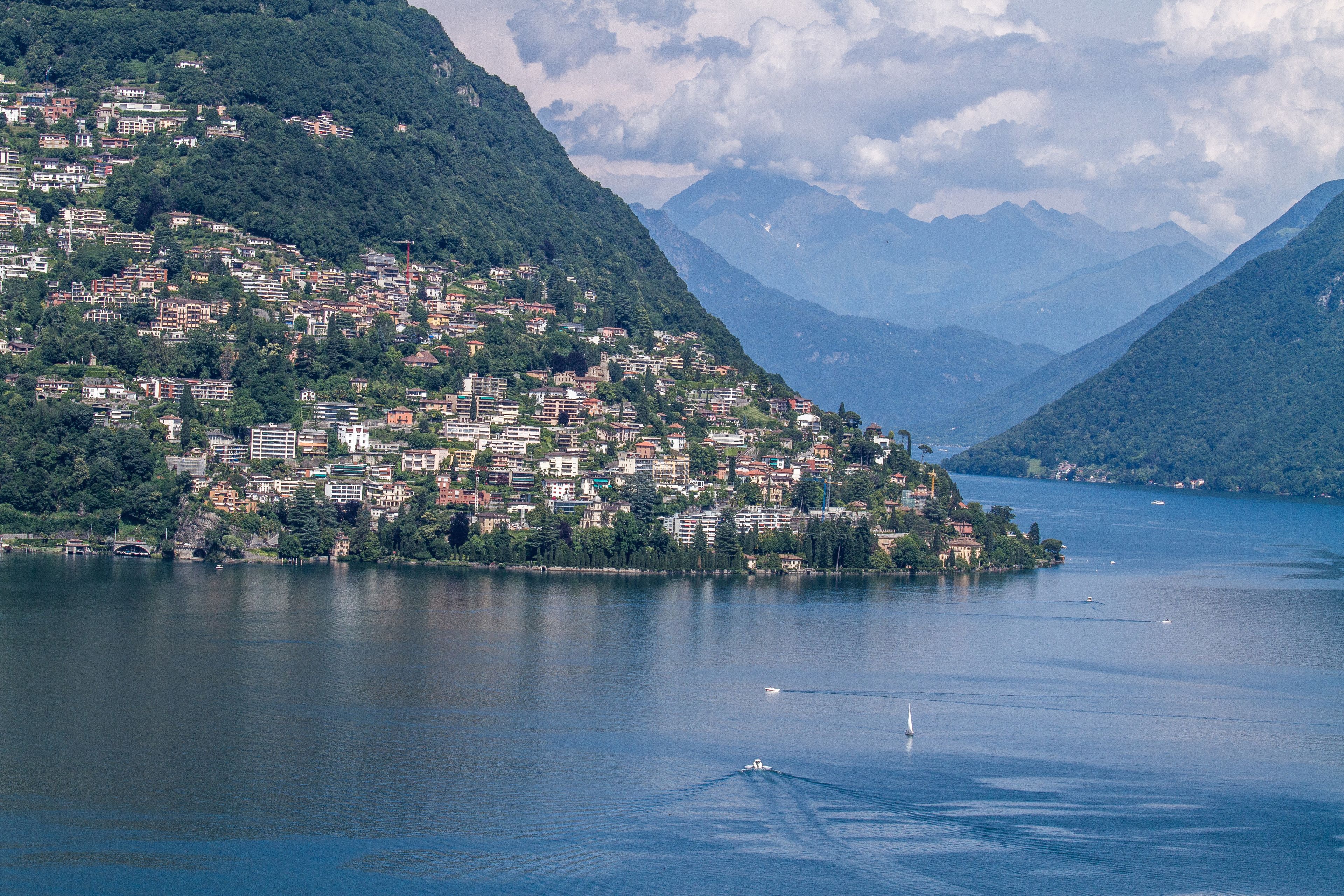 A lakeside town with buildings on a hillside, a clear view of the lake, and mountains in the background.