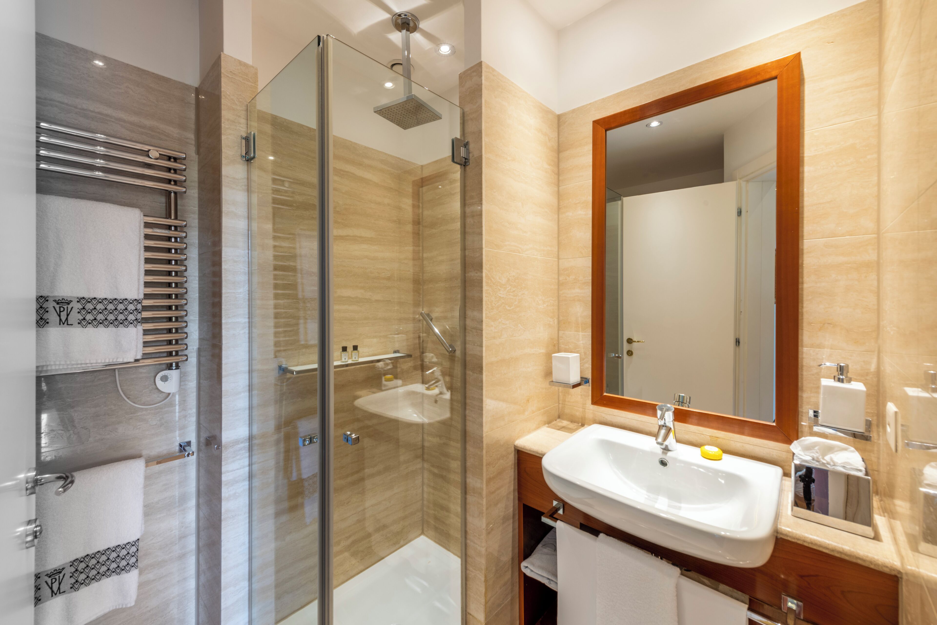 A modern bathroom with a glass-enclosed shower, a sink with a mirror, and towel racks.