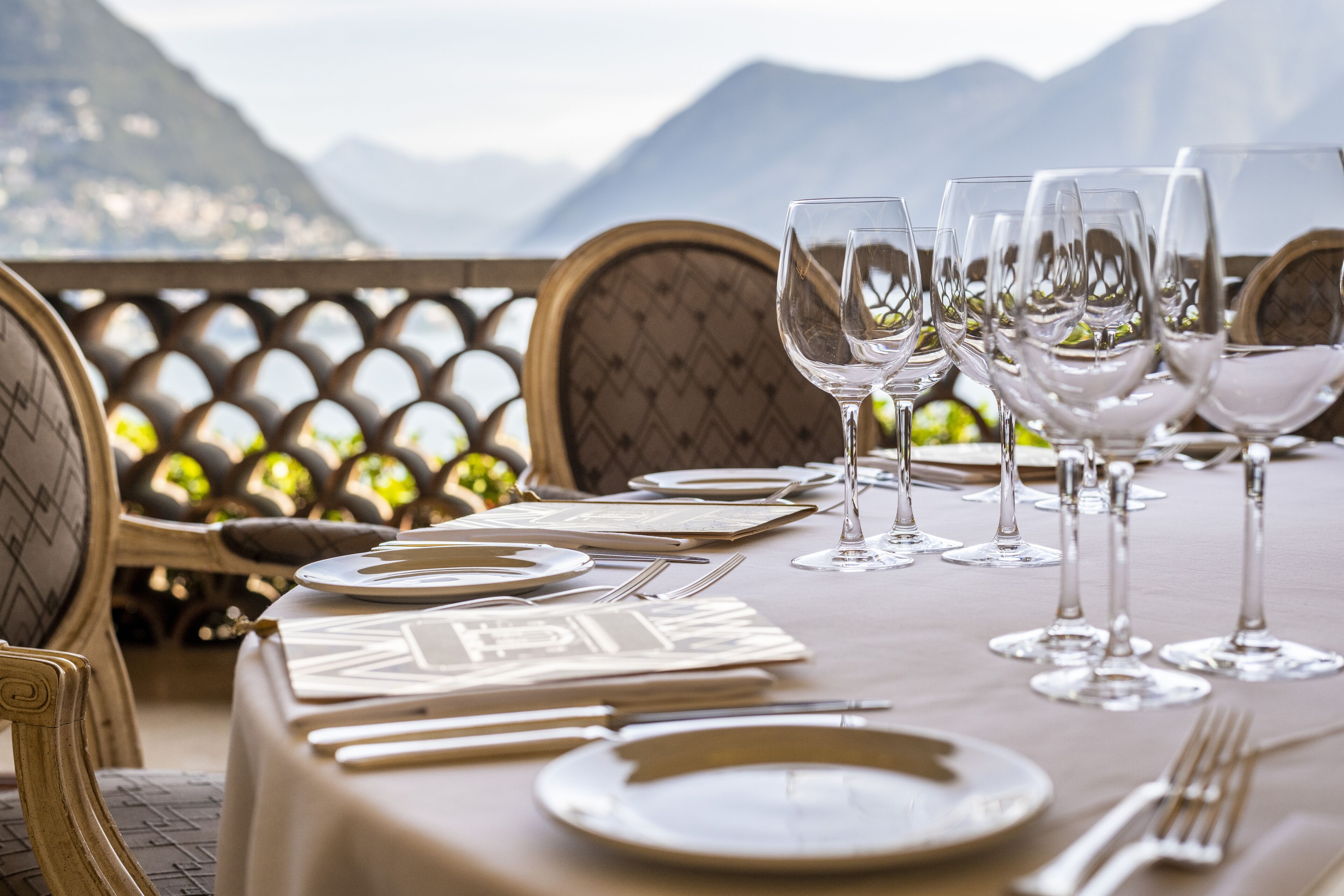 A table set for dining with wine glasses, plates, and cutlery, overlooking a mountainous landscape.