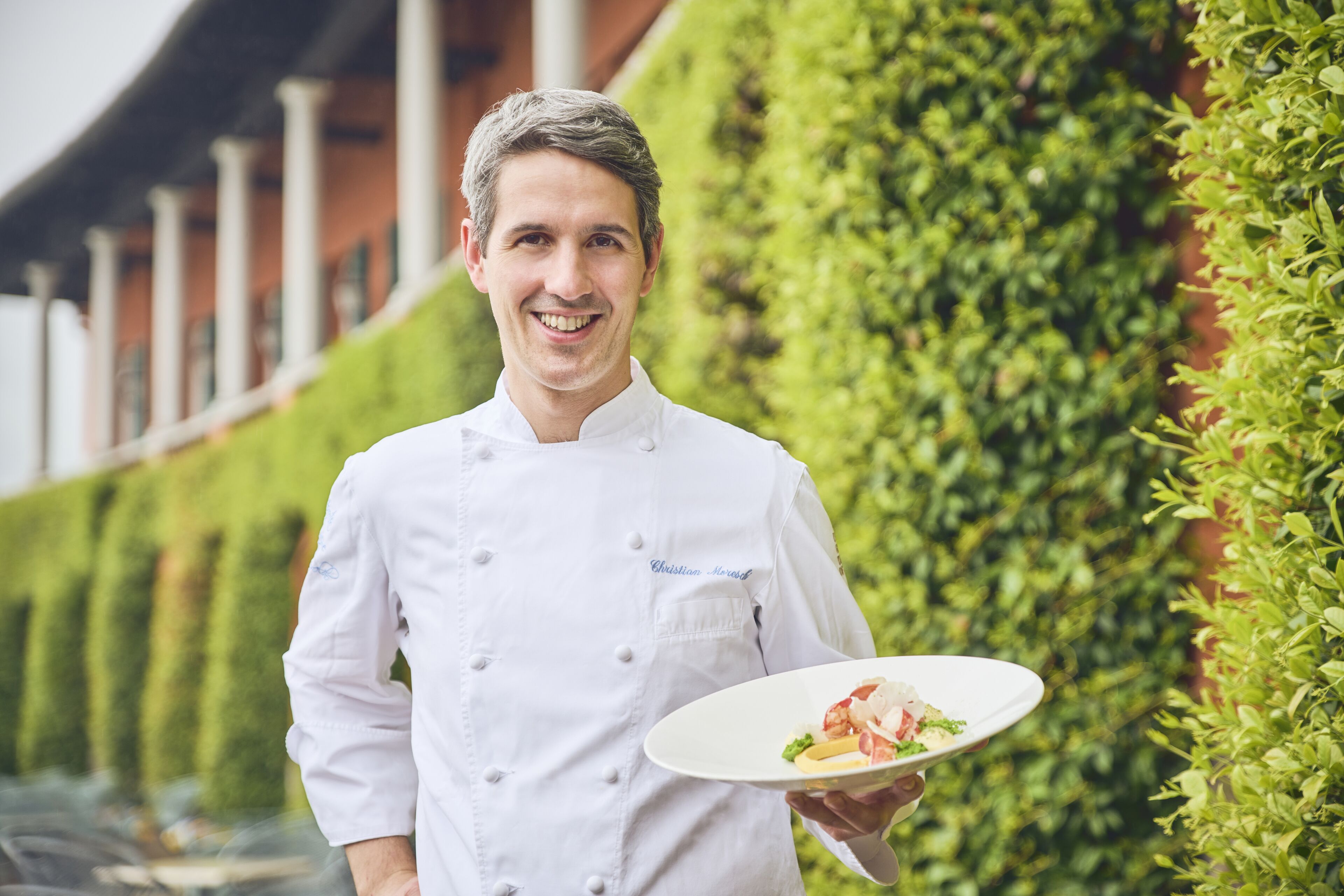 Ein Koch in einer weißen Uniform hält einen Teller mit Essen.
