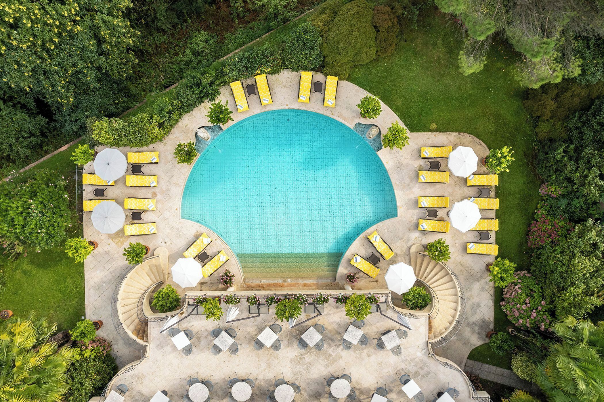 An aerial view of a resort with a central swimming pool, sun loungers, and a staircase leading to a terrace.