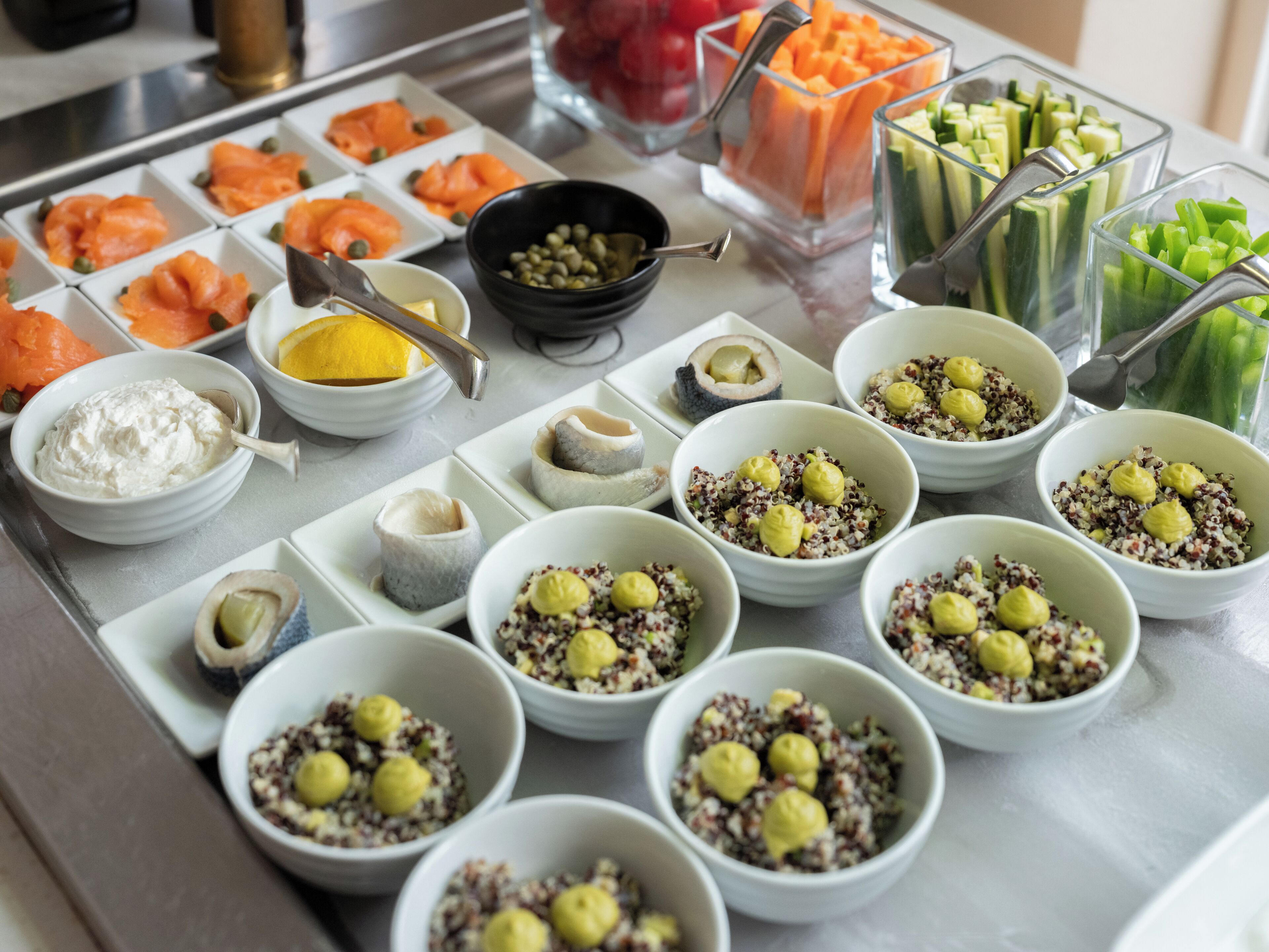 Un bufé con diversas opciones de comida, incluyendo salmón, verduras y tazones de quinua con bolitas amarillas.