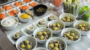 Un bufé con diversas opciones de comida, incluyendo salmón, verduras y tazones de quinua con bolitas amarillas.