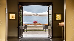 An open doorway leading to a terrace with outdoor seating and umbrellas, a Rolex watch display, and a view of a body of water.