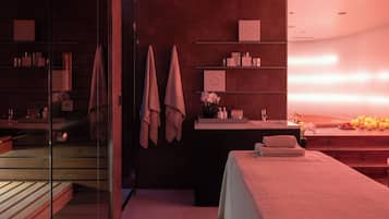 A modern spa room with a glass shower enclosure, a reception desk, and a massage table.