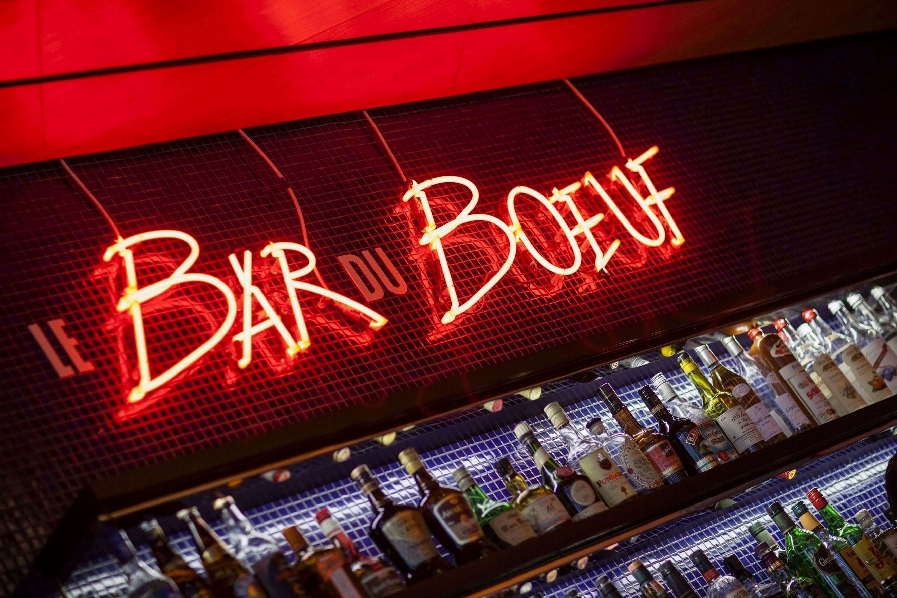 A bar with a neon sign reading "Bar du Bois" and shelves stocked with various liquor bottles.