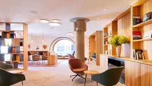 Et moderne interiør med et centralt siddeområde, træbogreoler og udsigt til en restaurant.