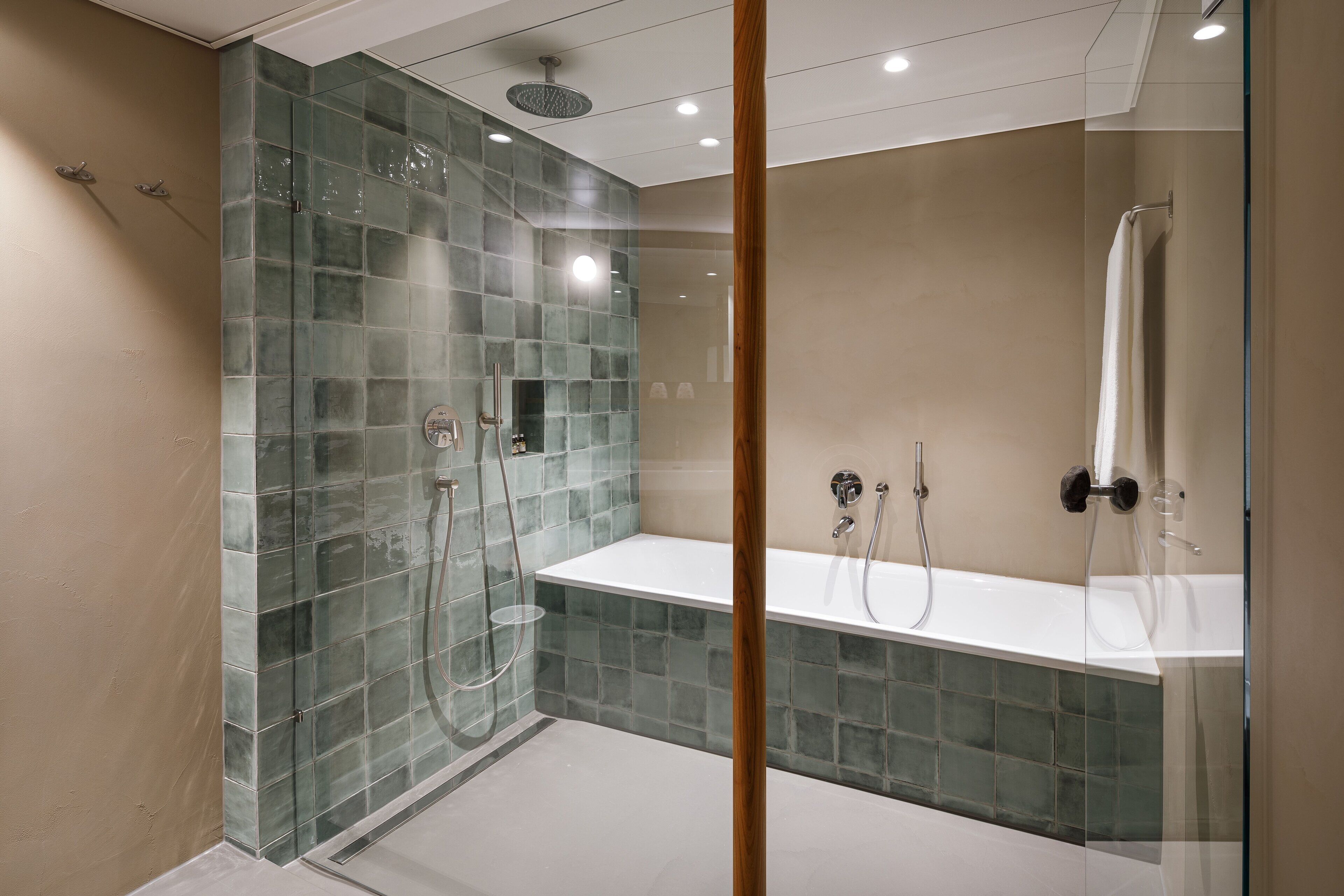 A modern bathroom with a glass-enclosed shower, a white bathtub, and a glass partition.