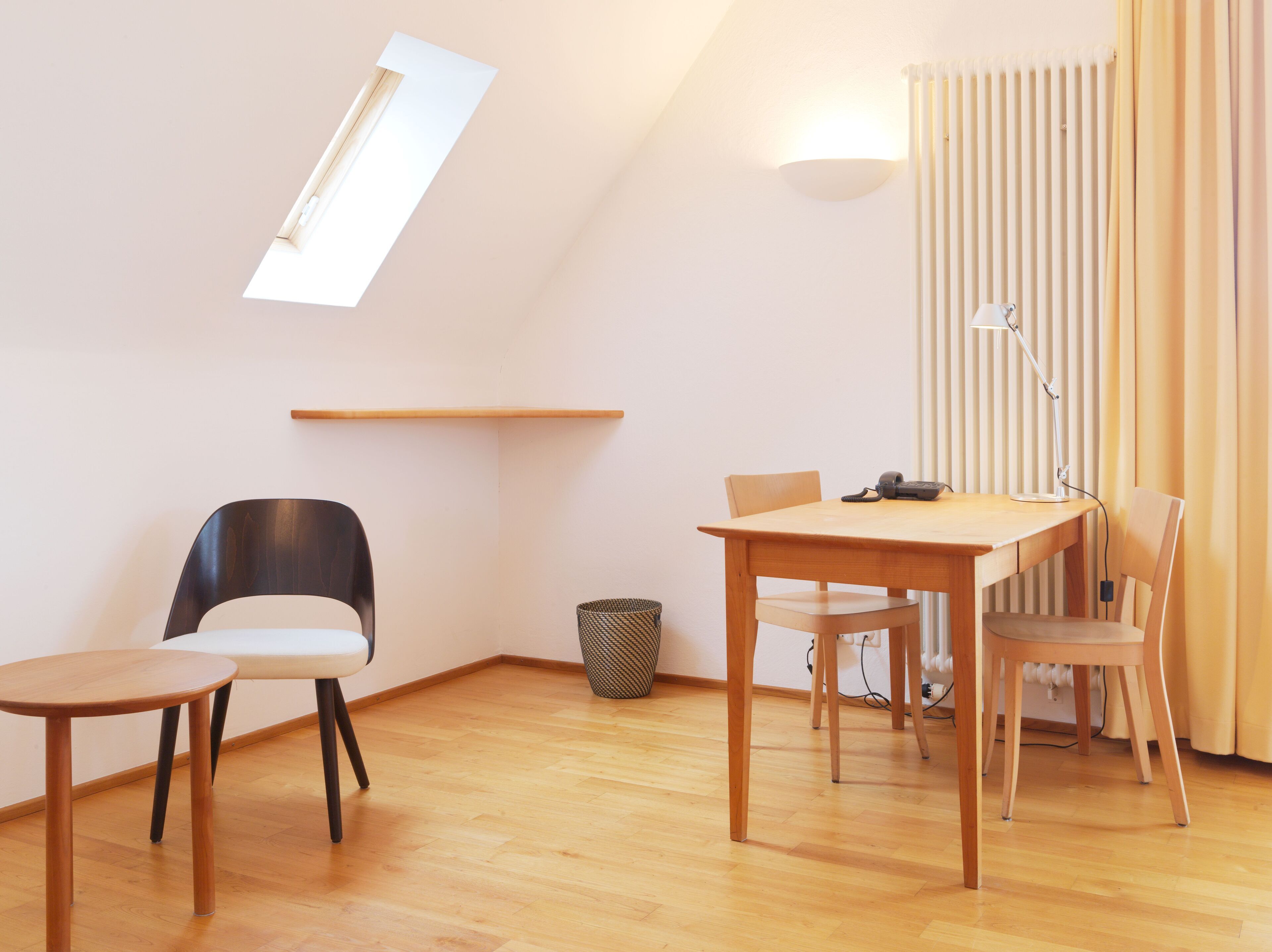 A modern, well-lit room with a sloped ceiling, a dining table with chairs, a small side table, and a lamp.