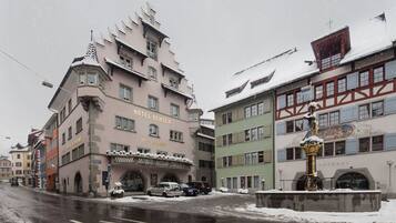 Un hôtel de style architectural européen traditionnel, caractérisé par une entrée d’angle remarquable et une façade recouverte de neige.