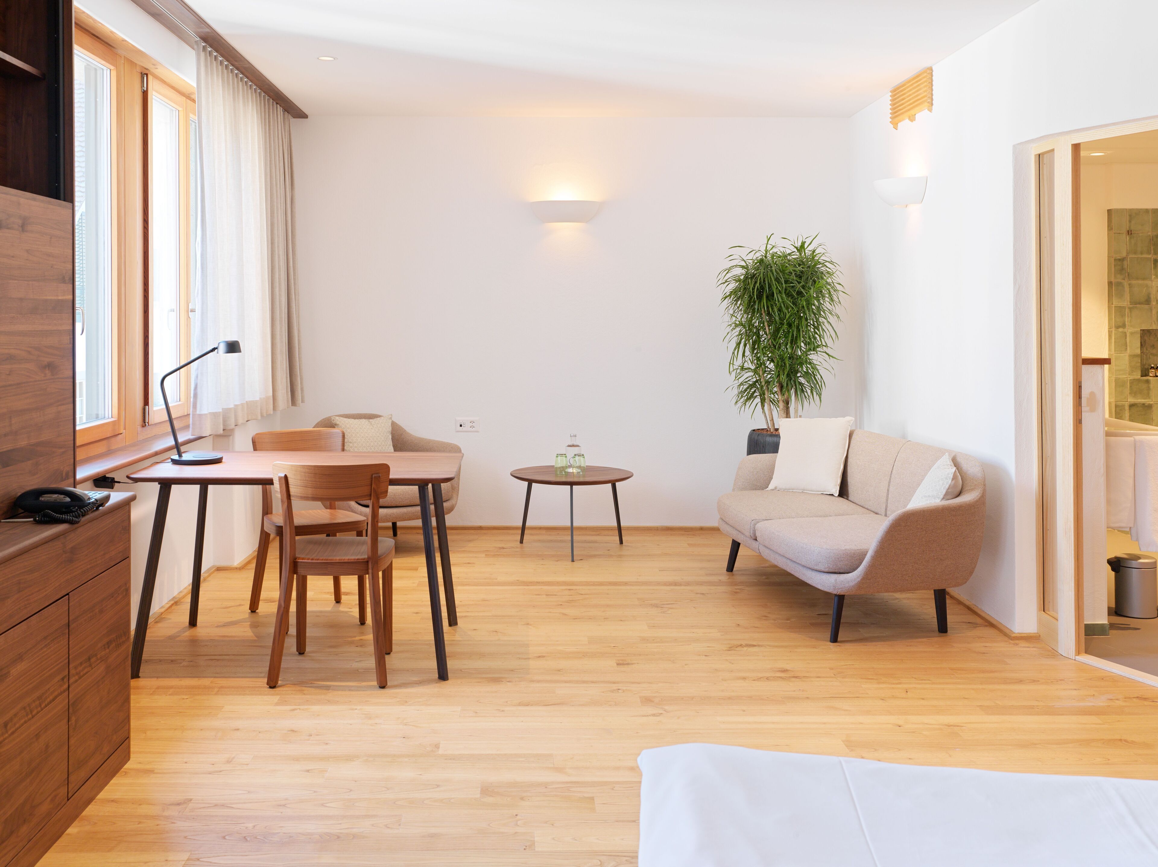 A modern living room with a wooden floor, a round dining table, a sofa, and a potted plant.